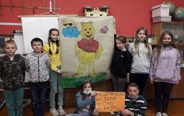 Ośmioro uczni&oacute;w prezentuje plakat z Kubusiem Puchatkiem podczas obchod&oacute;w Międzynarodowego Dnia Postaci z Bajek