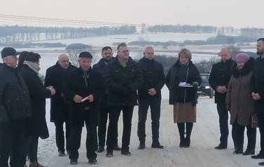 Grupa zaproszonych gości i ksiądz stoją na nowej nawierzchni drogi