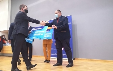 Mężczyna wręczający drugiemu mężczyźnie czek - nagrodę 