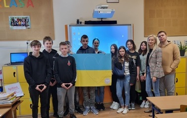 Grupa dzieci stojąca na tle tablicy w klasie lekcyjnej, prezentujaca flagę Ukrainy