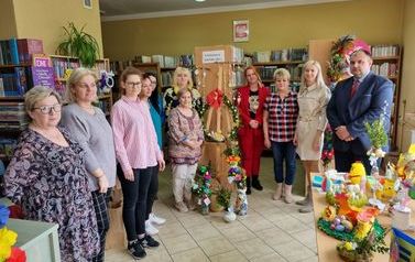 Grupa os&oacute;b na tle bibliotecznych p&oacute;łek z książkami