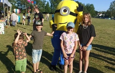 czworo dzieci stoi przy maskotce minionka