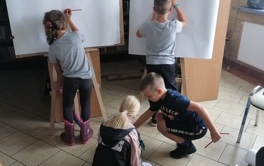 Czw&oacute;rka dzieci, dwoje rysuje przy tablicach, dwoje bawi się na podłodze