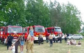 Uczestnicy imprezy na tle samochod&oacute;w pożarniczych