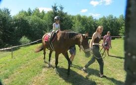 dziecko siedzi na koniu, kobieta prowadzi konia