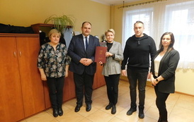 Trzy kobiety i dw&oacute;ch mężczyzn eksponują teczkę z podpisaną umową 