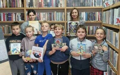 Grupa dzieci prezentuje książki w bibliotece 